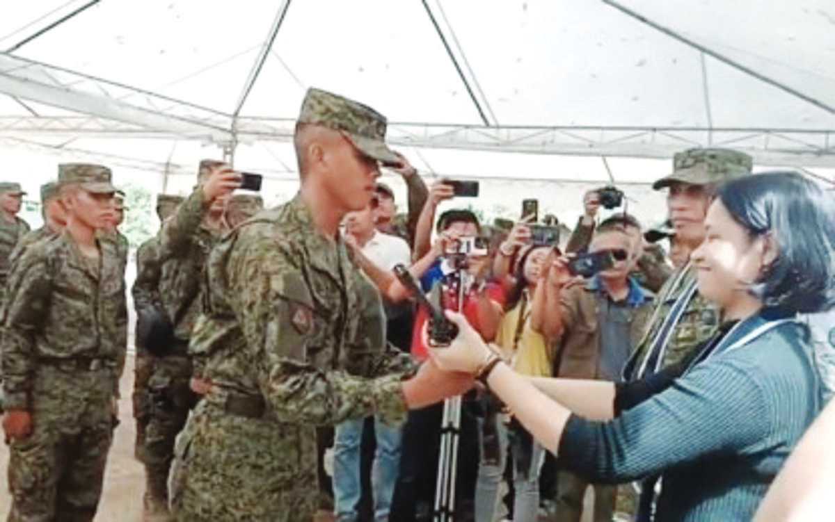 A Citizen Armed Force Geographical Unit Active Auxiliary member receives a service firearm from Director Christina Loren Umali of the Office of the Presidential Adviser on Peace, Reconciliation and Unity during the closing ceremony of their basic military training held at the 62nd Infantry Battalion headquarters in Negros Occidental’s Isabela town yesterday, November 17, 2023. A total of 64 civilian volunteers assigned to the patrol bases of various line battalions in Negros Island completed the six-week training. (62nd IB / Facebook video screenshot)