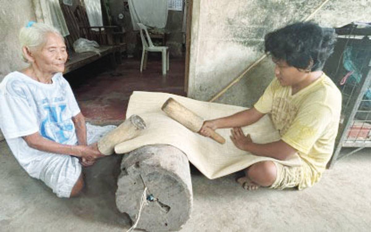 Antonia Indog Waro, 85 years old, and her grandson, Jerrycon, of Valencia, Negros Oriental, demonstrate the manual process of "pakang-pakang" for a smoother abaca fiber texture. The Fiber Industry Development Authority says that abaca production has declined over the years, prompting new interventions to strengthen the industry. (PNA photo)